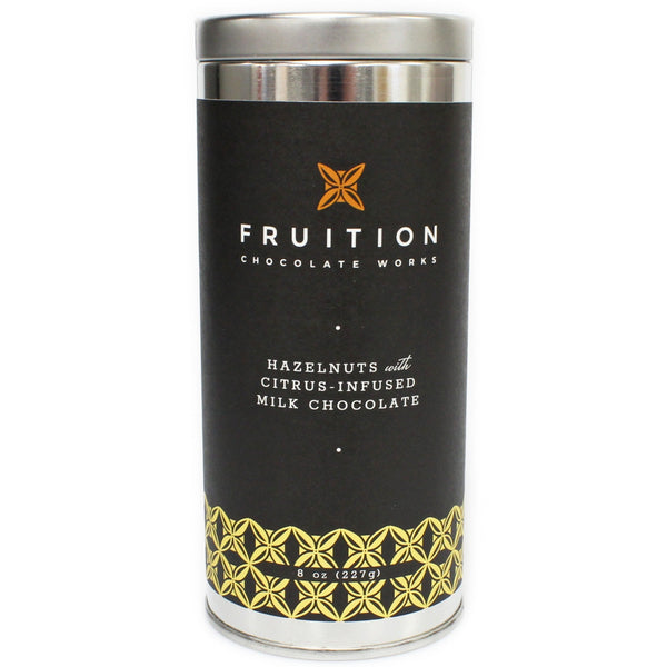 tall narrow metal tin with a black label with yellow pattern along the bottom. The label reads "fruition chocolate works: hazelnuts with citrus infused milk chocolate"