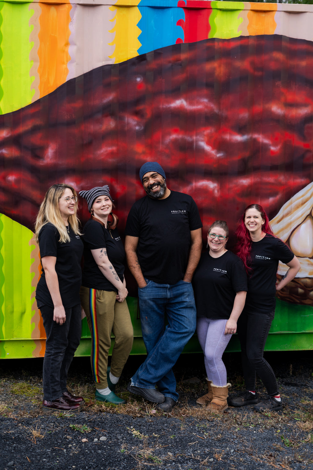 five people standing together and laughing, all wearing black shirts that say fruition chocolate works on the front