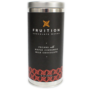 tall narrow metal tin with a black label with reddish pattern along the bottom. The label reads "fruition chocolate works: pecans with maple cinnamon milk chocolate"